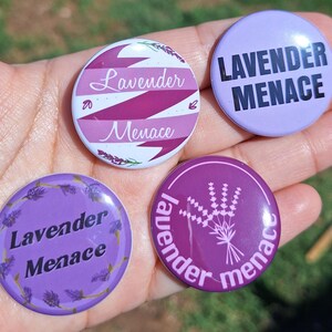 May include: Four round buttons with the text "Lavender Menace" in various designs. One button is light purple with black text. Another has a lavender sprig design. The other two buttons have the text "Lavender Menace" with lavender and white accents.