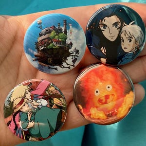 May include: Four round buttons with different images from the animated film 'Howl's Moving Castle'. The first button features a close-up of Howl and Calcifer, the second button features a close-up of the moving castle, the third button features a close-up of the fire demon, and the fourth button features a close-up of Sophie and Howl.