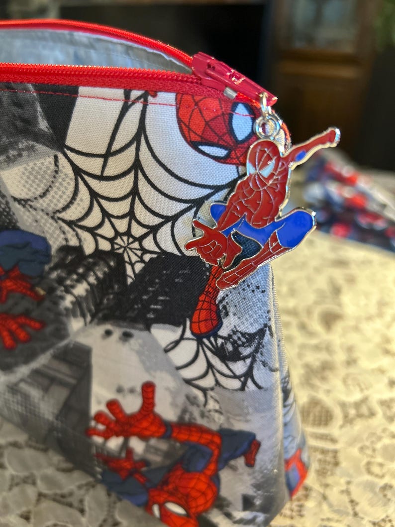 Puede incluir: Una bolsa con cremallera con tem&aacute;tica de Spider-Man. La tela muestra un patr&oacute;n de Spider-Man, telara&ntilde;as y paisajes urbanos en rojo, negro, blanco y azul. Una cremallera roja y un dije de Spider-Man completan el dise&ntilde;o.
