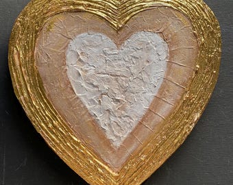 May include: A heart-shaped wooden wall art piece with a white heart in the center, surrounded by a gold and peach-colored border.