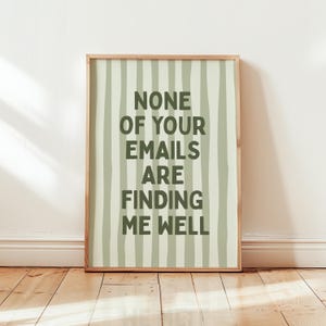 Può includere: Una stampa artistica rettangolare in una cornice di legno chiaro con uno sfondo verde pallido e strisce verticali verde scuro. Il testo in lettere maiuscole verde scuro recita: NONE OF YOUR EMAILS ARE FINDING ME WELL, centrato sulla stampa.
