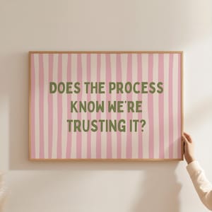 Może przedstawiać: Prostokątny obraz ścienny w jasnej drewnianej ramie z tłem w pionowe jasnoróżowe i białe paski. Tekst "DOES THE PROCESS KNOW WE'RE TRUSTING IT?" jest nadrukowany na środku pogrubioną, ciemnooliwkową czcionką bezszeryfową.