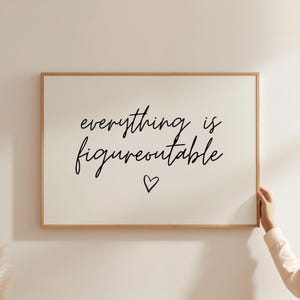 May include: A framed print featuring the phrase "everything is figureoutable" in black script, with a small heart beneath. The frame is light brown, and the background is off-white.