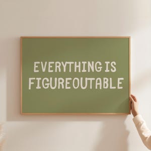 May include: A framed print with the text "EVERYTHING IS FIGUREOUTABLE" in white letters on a green background. The frame is made of light brown wood. The print is hanging on a white wall.