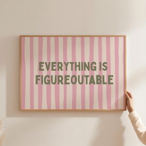 May include: A framed print with a pink and white striped background. The text "EVERYTHING IS FIGUREOUTABLE" is in green block letters. The frame is a light brown color.