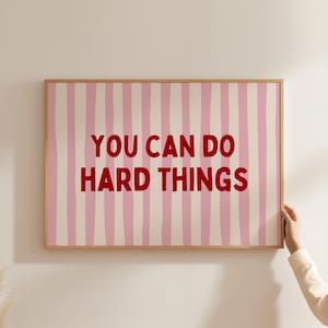 Peut inclure: Une affiche encadrée avec un fond à rayures roses et blanches. Le texte rouge vif dit "YOU CAN DO HARD THINGS". L'œuvre est dans un cadre en bois.
