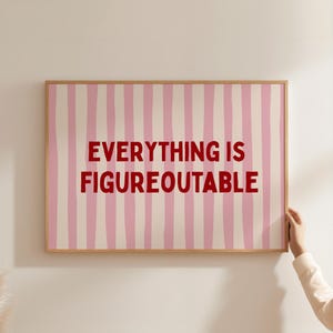 Könnte beinhalten: Ein gerahmter Druck mit einem rosa-weiß gestreiften Hintergrund und den Worten "EVERYTHING IS FIGUREOUTABLE" in Rot. Der Rahmen hat eine hellbraune Farbe.
