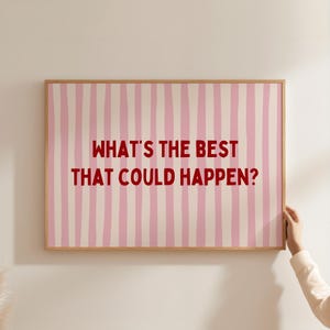 Könnte beinhalten: Ein rechteckiger Wandkunstdruck in einem hellen Holzrahmen mit einem Hintergrund aus vertikalen rosa und weißen Streifen. Der Text "WHAT'S THE BEST THAT COULD HAPPEN?" ist in fetten, dunkelroten Großbuchstaben in der Mitte gedruckt.