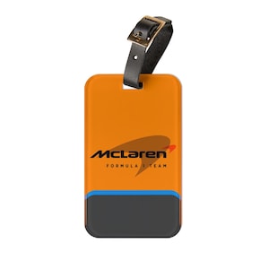 May include: Orange luggage tag with a black McLaren Formula 1 Team logo. The tag has a black leather strap with a gold buckle.