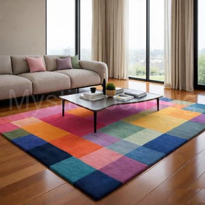 Könnte beinhalten: Ein farbenfroher Teppich mit einem geometrischen Muster aus großen Quadraten in Rosa, Orange, Gelb, Grün, Blau und Lila. Der Teppich liegt in einem Wohnzimmer mit einem neutralen Sofa und einem Couchtisch.
