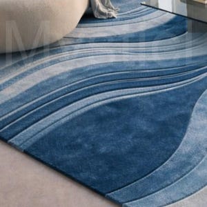 Modern blue abstract hand-tufted wool area rug with wave design placed in a luxury contemporary living room with sofa and glass table.
