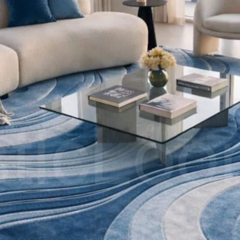 Modern blue abstract hand-tufted wool area rug with wave design placed in a luxury contemporary living room with sofa and glass table.