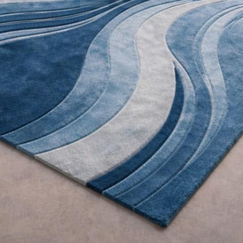 Modern blue abstract hand-tufted wool area rug with wave design placed in a luxury contemporary living room with sofa and glass table.