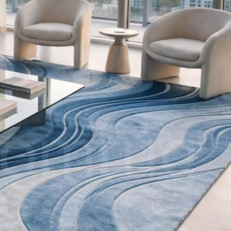 Modern blue abstract hand-tufted wool area rug with wave design placed in a luxury contemporary living room with sofa and glass table.