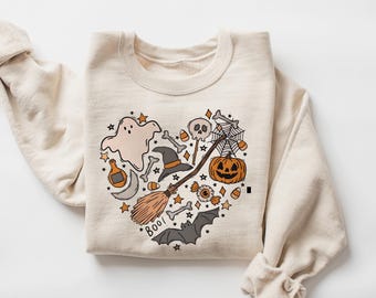 Könnte beinhalten: Cremefarbenes Sweatshirt mit einem herzförmigen Halloween-Motiv. Die Grafik zeigt einen Geist, einen Hexenhut, einen Besen, einen Kürbis, eine Fledermaus und das Wort "Boo!". Das Design hat orange, schwarze und beige Farben.