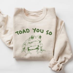 May include: A beige sweatshirt with the text "TOAD YOU SO" printed in green. A green cartoon toad is below the text.