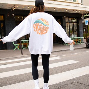 May include: White sweatshirt with a graphic of a sunset and the text "FOREVER CHASING SUNSETS".