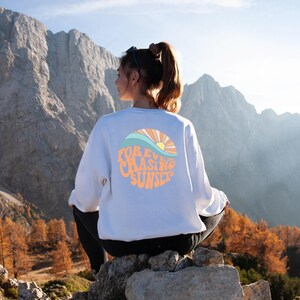 May include: A white sweatshirt with a graphic design of a sunset and waves. The text on the graphic says "FOREVER CHASING SUNSETS".