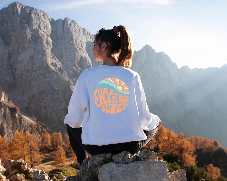 May include: A white sweatshirt with a graphic design of a sunset and waves. The text on the graphic says "FOREVER CHASING SUNSETS".