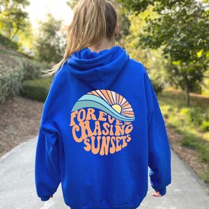 May include: A royal blue hoodie with a graphic of a sunset and waves on the back. The graphic says "FOREVER CHASING SUNSETS" in a retro font.