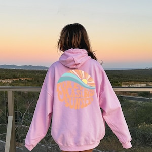 May include: Pink hoodie with a graphic of a sunset and waves with the text "Chasing Sunset".