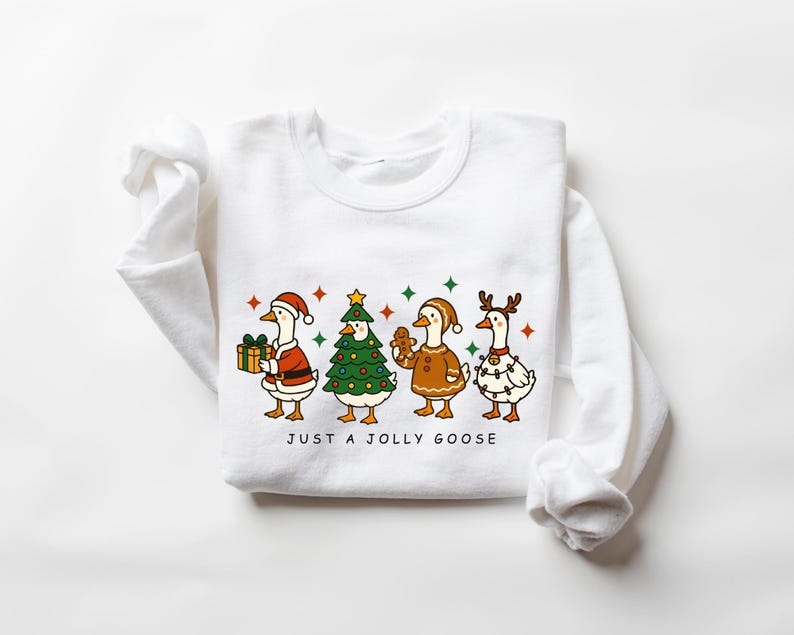 May include: White sweatshirt featuring a festive illustration of four geese dressed for Christmas. One goose holds a gift, another is a Christmas tree, a third is a gingerbread cookie, and the last is decorated with lights. The text "JUST A JOLLY GOOSE" is below the geese.