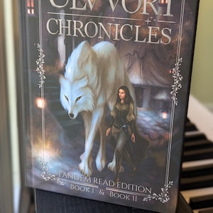 May include: A hardcover book titled The Ulvvori Chronicles by R.H. Linehan, Tandem Read Edition Book I & Book II. The cover features a large white wolf walking beside a person in dark clothing, set against a dark, atmospheric background with glowing lights.