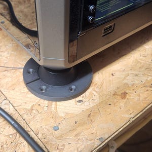 May include: A close-up of the bottom of a black computer case with a black plastic foot. The foot has four screw holes and a small groove.