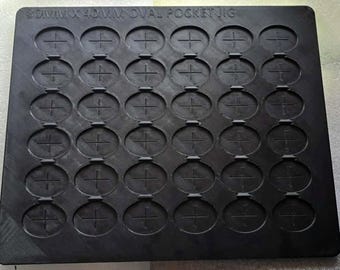 May include: A black rectangular 50mm x 40mm oval pocket jig featuring a grid of thirty recessed oval cavities. Each oval cavity contains a centered cross-shaped indentation. The text 50MM X 40MM OVAL POCKET JIG is embossed along the top edge.