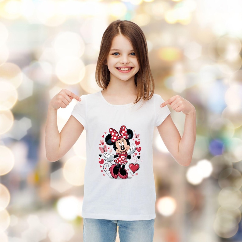 May include: A white short-sleeved t-shirt featuring a graphic print of Minnie Mouse wearing a red and white polka dot dress and bow, surrounded by red and pink hearts and small butterflies, centered on the front of the garment.