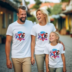May include: White t-shirts with a colourful cartoon graphic of Spider-Man and other characters. The graphic includes a blue spiderweb, and red, black, and blue figures. The shirts are worn by a family.