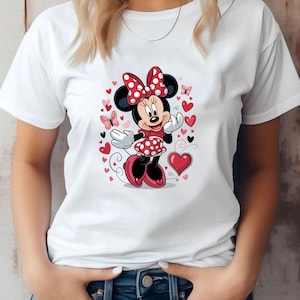 May include: A white short-sleeved t-shirt featuring a central graphic of Minnie Mouse wearing a red and white polka-dot dress and matching bow. The character is surrounded by various red and pink hearts and small butterflies on a white background.