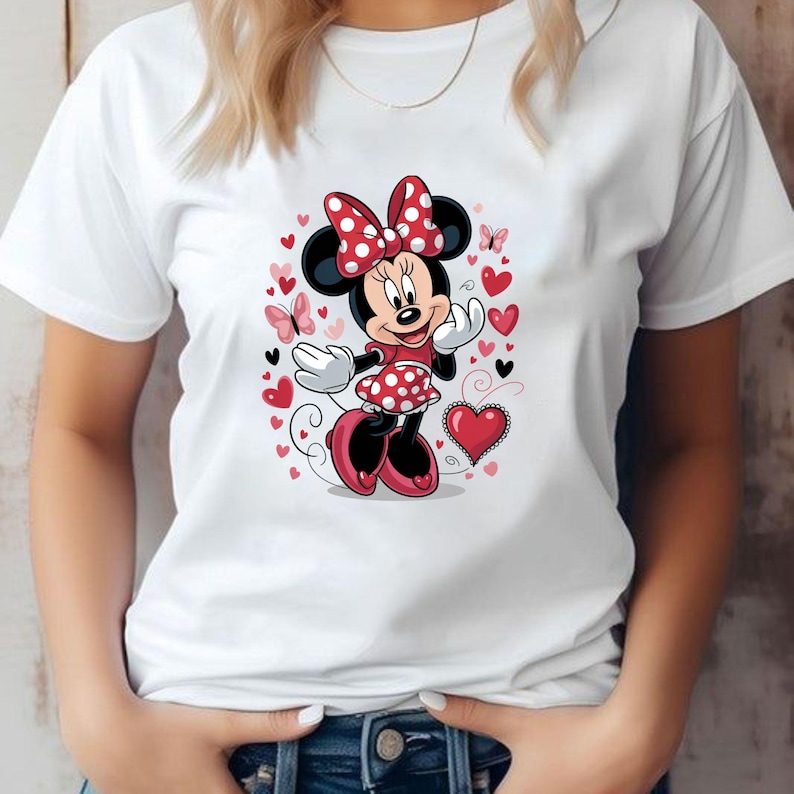 May include: A white short-sleeved t-shirt featuring a central graphic of Minnie Mouse wearing a red and white polka-dot dress and matching bow. The character is surrounded by various red and pink hearts and small butterflies on a white background.