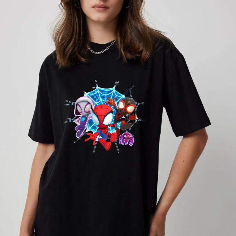 May include: Black t-shirt with a vibrant graphic of three Spider-Man characters set within a blue web. The characters are in red, black, and white costumes. A purple spider is also included in the design. The shirt is made of a soft material.