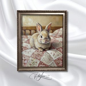 May include: A framed print of a bunny rabbit. The artwork depicts a light brown bunny with pink accents, resting on a pink and white quilt. The frame is a gold color. The print is signed "Paul Lewis Prints".
