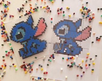 May include: A completed blue and pink bead art of the character Stitch, next to a pattern guide. The word "Stitch" is printed on the pattern guide. Scattered around are various colored beads, used for the art project.