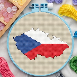 Pode incluir: Um bastidor de bordado em ponto cruz com a bandeira da República Tcheca. A bandeira, em azul, branco e vermelho, é bordada em tecido bege. O bastidor azul claro é rodeado por materiais de artesanato, como linha e botões.