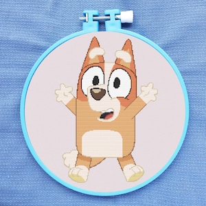 May include: A cross-stitch embroidery hoop with a cartoon image of a brown and white dog with big eyes and a surprised expression. The dog is standing with its arms outstretched.