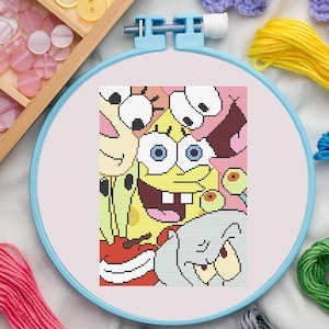 Könnte beinhalten: Eine Kreuzstich-Stickerei mit einem farbenfrohen Design von SpongeBob Schwammkopf und anderen Charakteren aus der Zeichentrickserie. Das Kunstwerk befindet sich in einem hellblauen Stickrahmen, umgeben von Bastelbedarf.