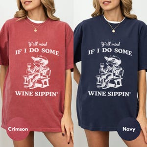 May include: Crimson and navy blue t-shirts with a white graphic of a frog in a cowboy hat, holding a wine glass, and the text "Y'all mind IF I DO SOME WINE SIPPIN'". The shirts are oversized.
