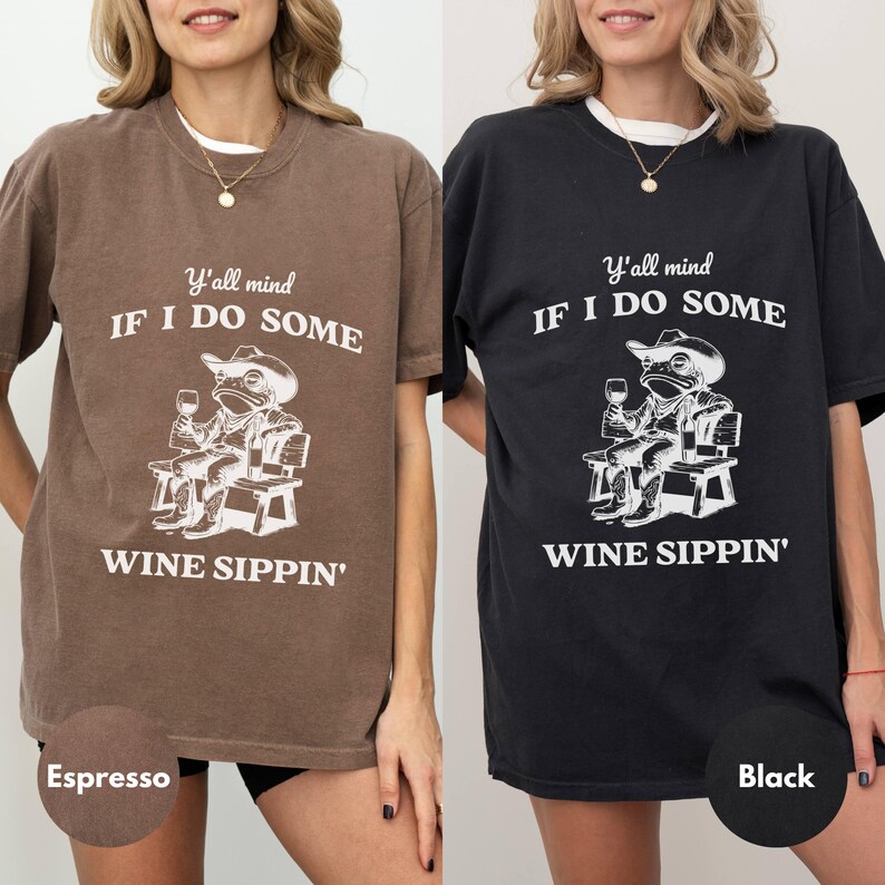 May include: Two t-shirts, one espresso and one black, featuring a frog wearing a cowboy hat, holding a wine glass, and sitting on a bench. The text reads "Y'all mind IF I DO SOME WINE SIPPIN'".