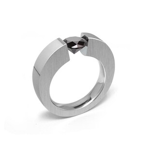 May include: A silver ring featuring a black gemstone set in the centre. The ring is crafted from smooth, brushed metal and boasts a distinctive, contemporary design.