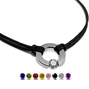 May include: A black cord necklace with a silver ring pendant featuring a clear gemstone. The ring is open on one side. The necklace is available with a variety of coloured gemstones, including blue, green, red, yellow, pink, black, white, and purple.