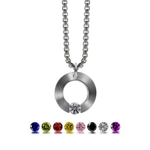May include: A silver chain necklace with a round pendant featuring a single clear gemstone. The pendant has a brushed metal finish and a circular opening. The necklace is shown with a selection of coloured gemstones, including blue, green, red, yellow, pink, black, white, and purple.
