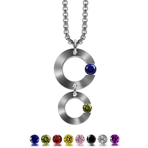 Peut inclure: Un collier en argent avec deux cercles liés, chacun avec une petite pierre précieuse. Le cercle supérieur a une pierre précieuse bleue, et le cercle inférieur a une pierre précieuse jaune. Le collier est présenté avec une variété d'autres couleurs de pierres précieuses.
