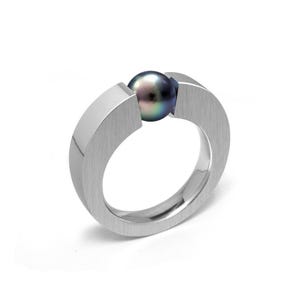 May include: A silver ring featuring a dark iridescent pearl set in the centre. The ring is crafted from smooth, brushed metal and boasts a modern, minimalist design.