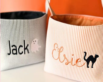 May include: Two fabric buckets with handles. The left bucket is white with thin black pinstripes, featuring the embroidered name Jack and a ghost icon. The right bucket is white with thin orange pinstripes, featuring the embroidered name Elsie and a black cat icon.