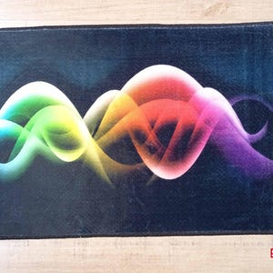 May include: A rectangular rug with a dark blue background and a vibrant, colorful design. The design features flowing, abstract shapes in shades of green, yellow, orange, pink, and purple. The rug has a black border and a "SAMPLE" stamp.