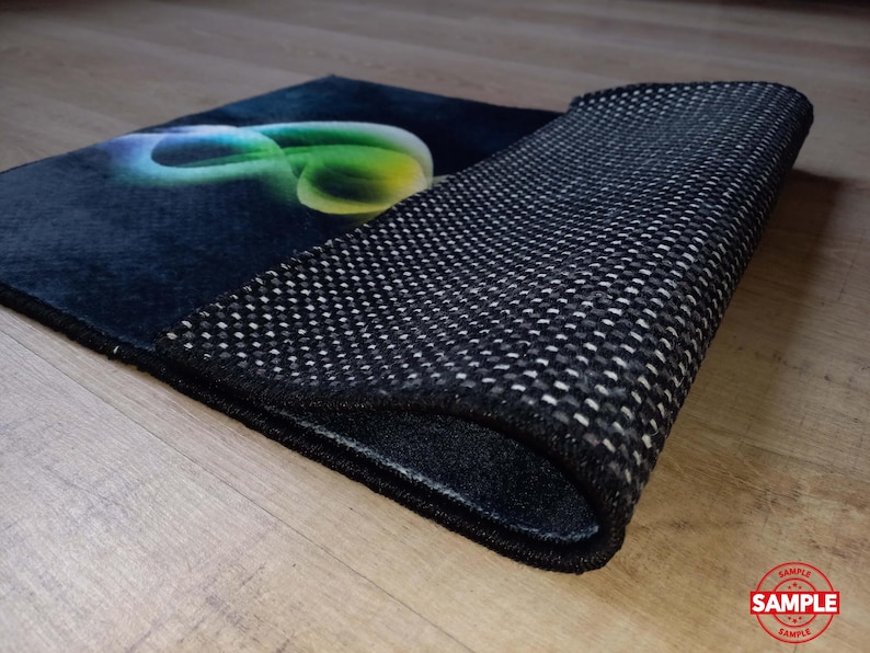 May include: A rectangular rug with a dark blue surface and a colorful, abstract design. The rug's underside is black with a textured, non-slip pattern. The rug is partially rolled up, revealing the underside.