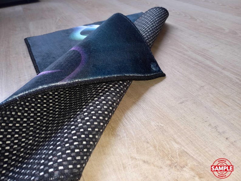 May include: A rolled-up, dark blue rug with a black border and a non-slip, checkered underside. The top surface features a design with blue, purple, and green hues. The rug is partially unrolled, revealing its texture and pattern.